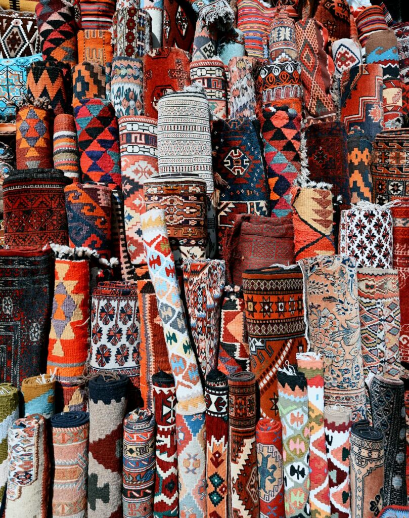 Photo d'un étal de souk marocain avec des tapis berbères colorés roulés et empilés, affichant une variété de motifs géométriques et traditionnels riches en couleurs