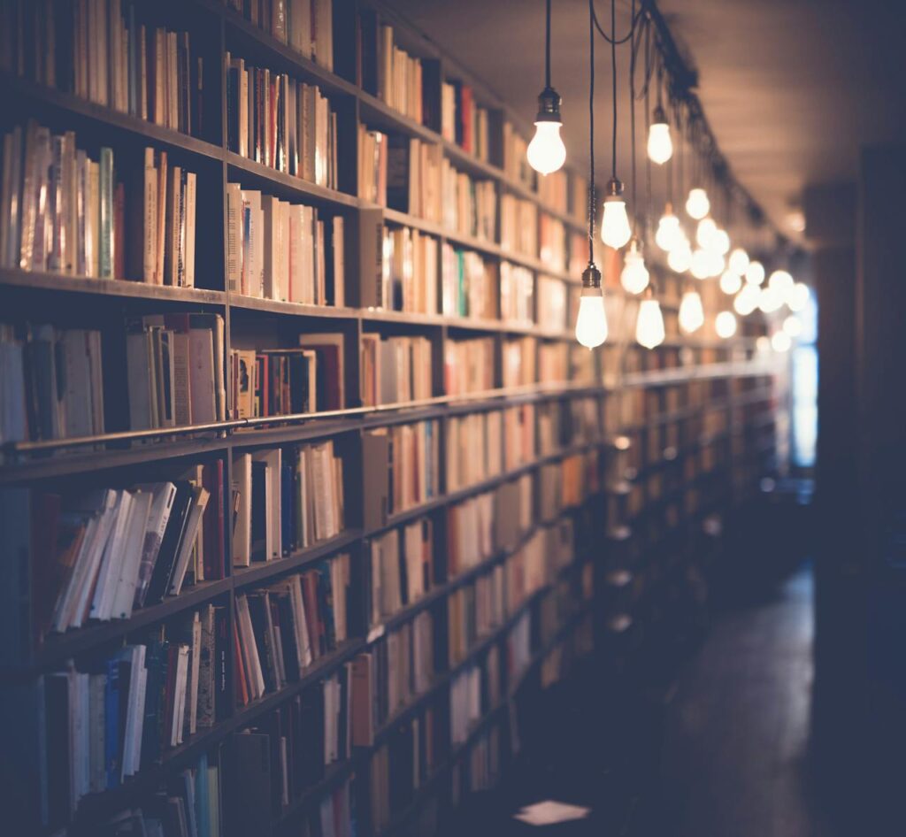 Photo d'une bibliothèque avec des étagères remplies de livres, éclairée par une série d'ampoules suspendues, créant une ambiance chaleureuse et studieuse