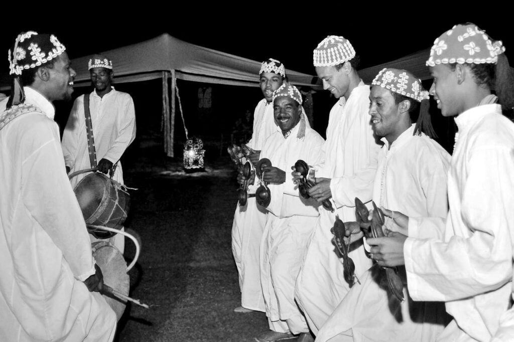 Artistes marocains en costumes traditionnels jouant des instruments de musique lors du Festival National des Arts Populaires de Marrakech, sous des tentes, la nuit.