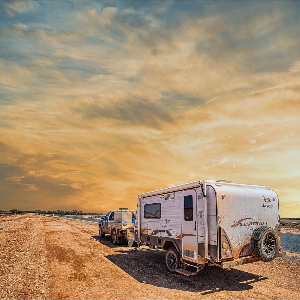 Cette image montre un magnifique voyage en camping-car au Maroc sous un ciel crépusculaire aux teintes orangées et dorées.
