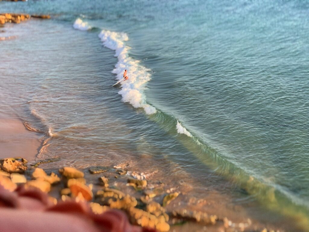 Cette image captivante présente un surfeur chevauchant une vague sur une plage côtière magnifique, probablement l'une des Meilleures plages près d’Agadir à Découvrir en 2025.