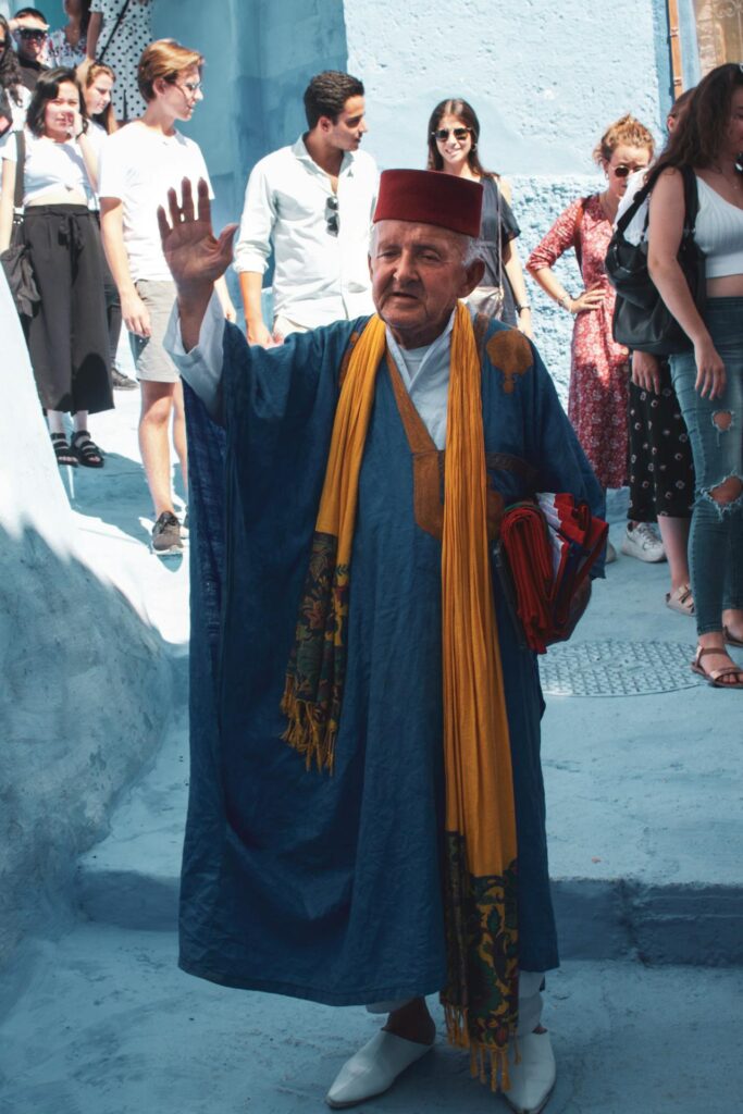 Une image vibrante d'un voyage organisé au Maroc, montrant un homme âgé vêtu d'une robe traditionnelle bleue ornée d'un foulard jaune,