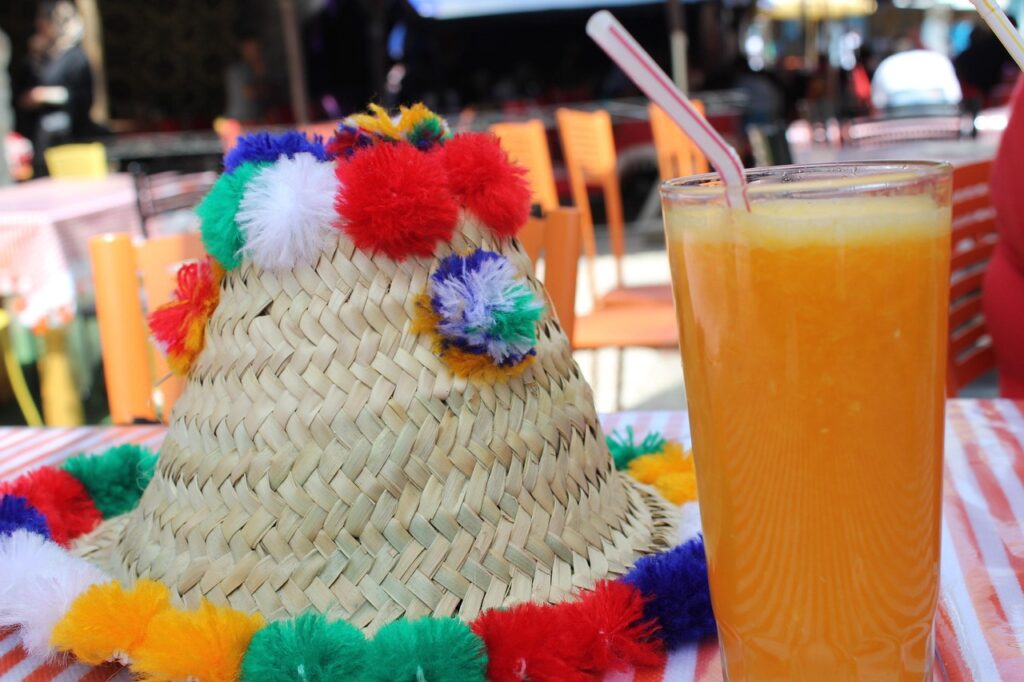 Une table colorée avec un chapeau traditionnel et un verre de jus d’orange frais, dans un cadre de café animé. Image illustre les aspects économiques d’un budget voyage au Maroc,