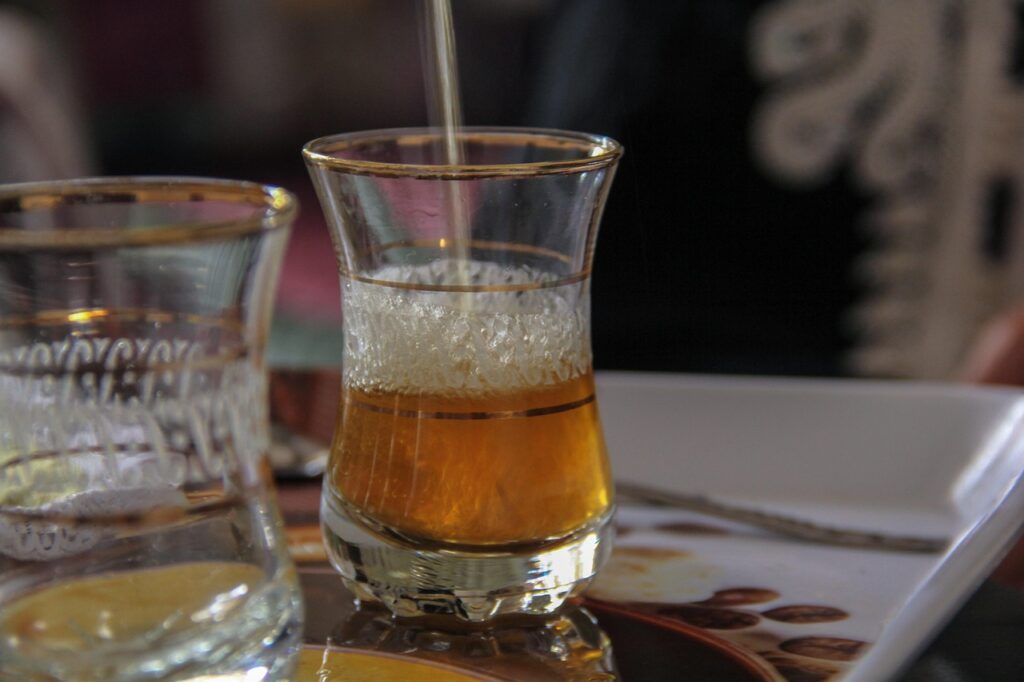 Une tasse en verre élégante remplie de thé à la menthe, versé traditionnellement, posée sur une table avec une autre tasse à côté. Cette scène reflète l’hospitalité marocaine idéal pour un budget voyage au Maroc