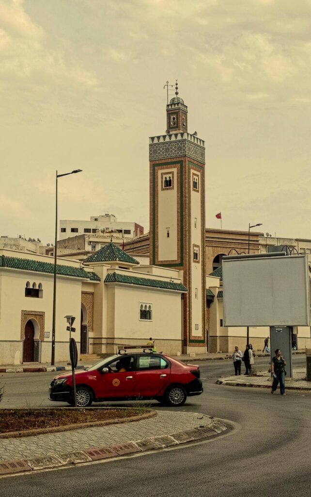 Scène typique des transports au Maroc : un petit taxi rouge circule devant une mosquée