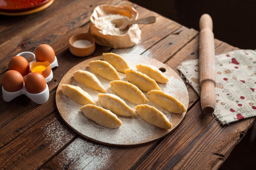 Sur une table en bois rustique et farinée, des pâtisseries marocaines non cuites, probablement des cornes de gazelle, sont délicatement disposées en rangées sur une planche ronde