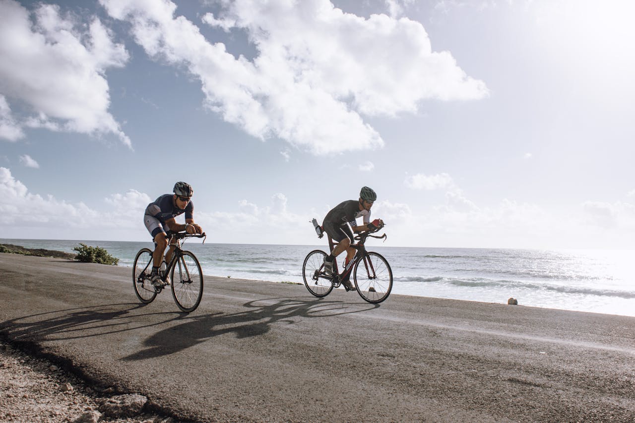 L'image montre deux cyclistes pédalant sur une route asphaltée longeant une plage. Cette scène illustre une aventure captivante du Maroc à vélo.