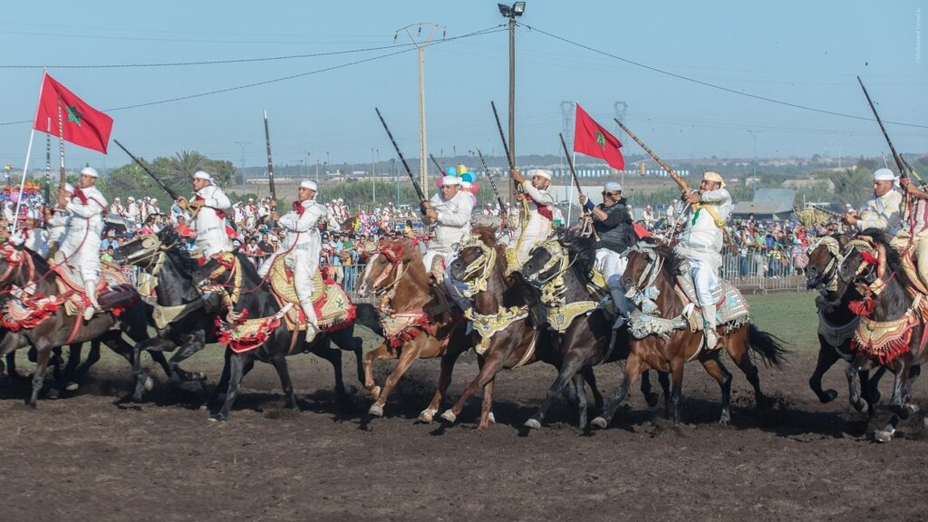 Une troupe de cavaliers participant à la Fantasia marocaine, vêtus de costumes traditionnels blancs ornés de rouge, chevauchant des chevaux richement décorés
