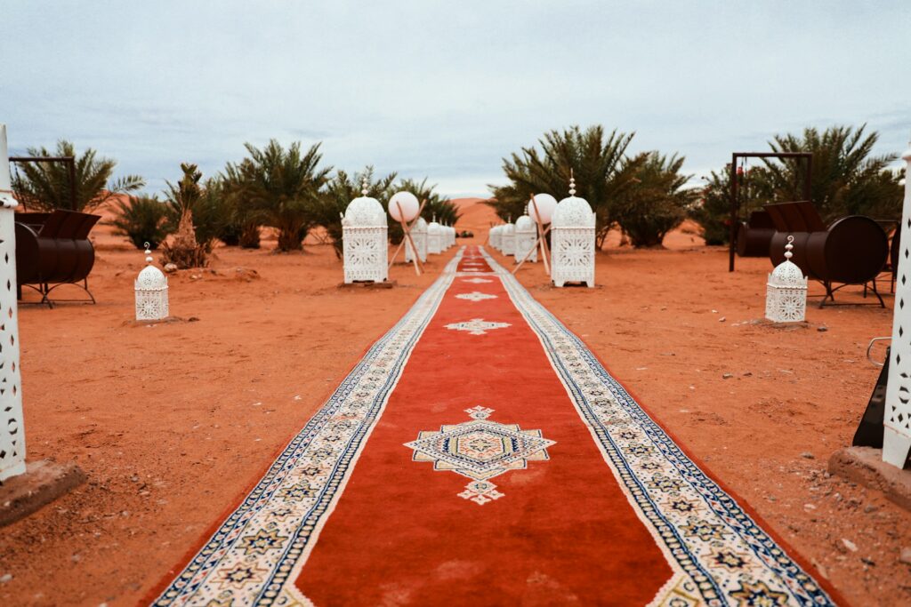 Une allée élégante dans un campement de Glamping de Luxe au Maroc, avec un tapis rouge orné de motifs traditionnels menant à des tentes luxueuses