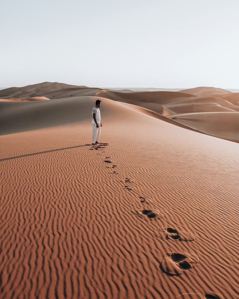 Homme en tenue blanche, debout seul sur une dune. Il s'apprête à explorer le Maroc en solo.