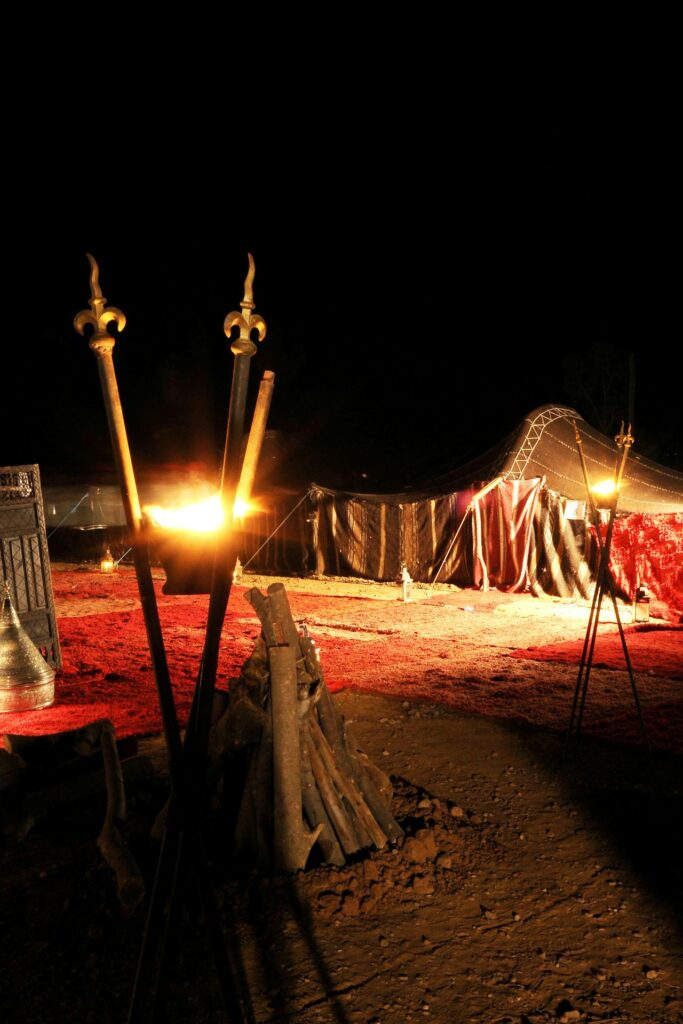 Une scène nocturne captivante pour explorer les alentours de Marrakech : un campement désertique illuminé par des torches flamboyantes et des lanternes