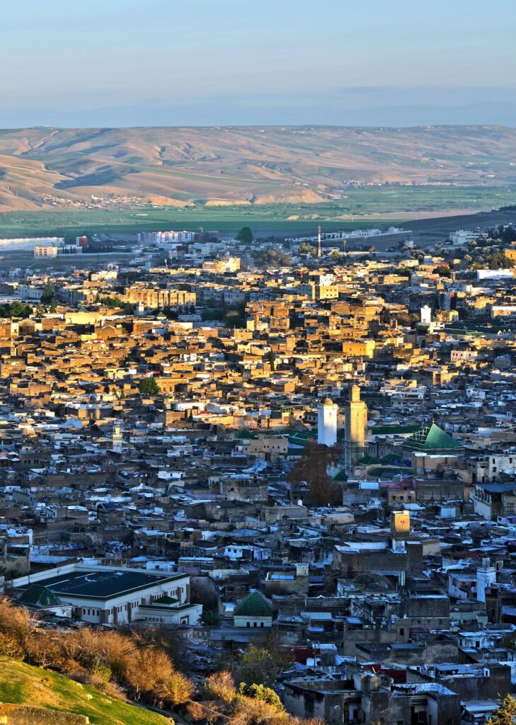 Cette image dévoile une vue spectaculaire de Fès authentique au lever du soleil, où la lumière dorée éclaire les toits en terrasse de la médina,