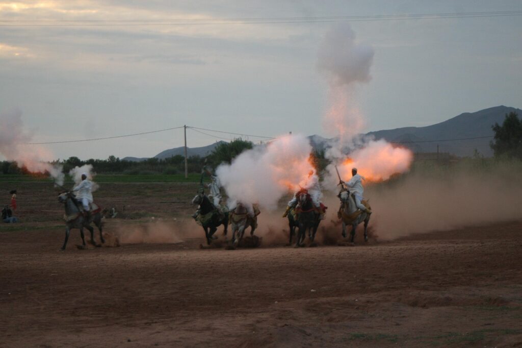 Une scène vibrante de la Fantasia marocaine avec des cavaliers, tirant de mousquets et créant des explosions de fumée et de feu,