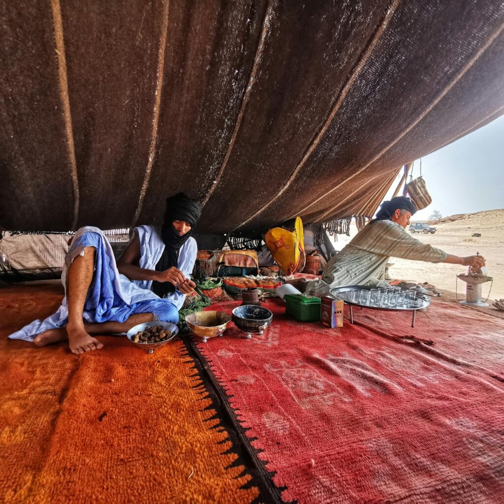 Intérieur d'une tente nomade au désert, avec deux personnes assises sur des tapis colorés. Voyager lentement pour des découvertes authentiques dans un cadre désertique paisible et accueillant