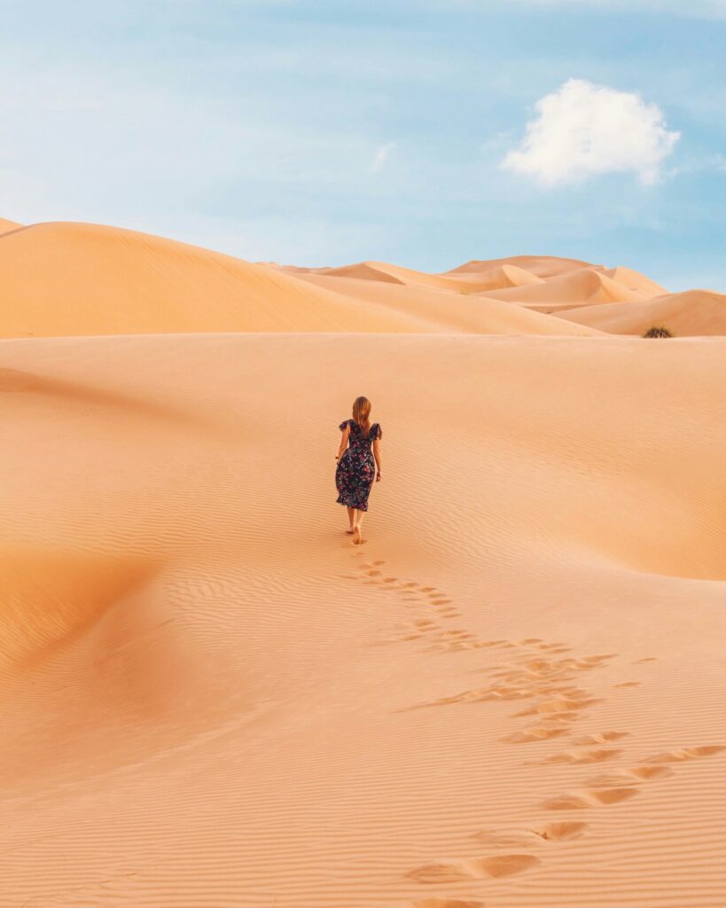 Une femme seule, portant une robe à motifs foncés, marchant pieds nus sur les dunes de sable lors de son aventure pour explorer le Maroc en solo