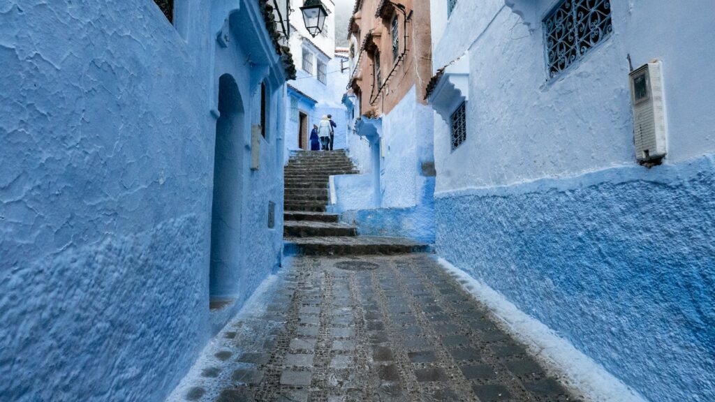 Découvrez le Maroc en été 2025 avec cette vue pittoresque d'une ruelle étroite de Chefchaouen, aux murs peints d'un bleu éclatant.