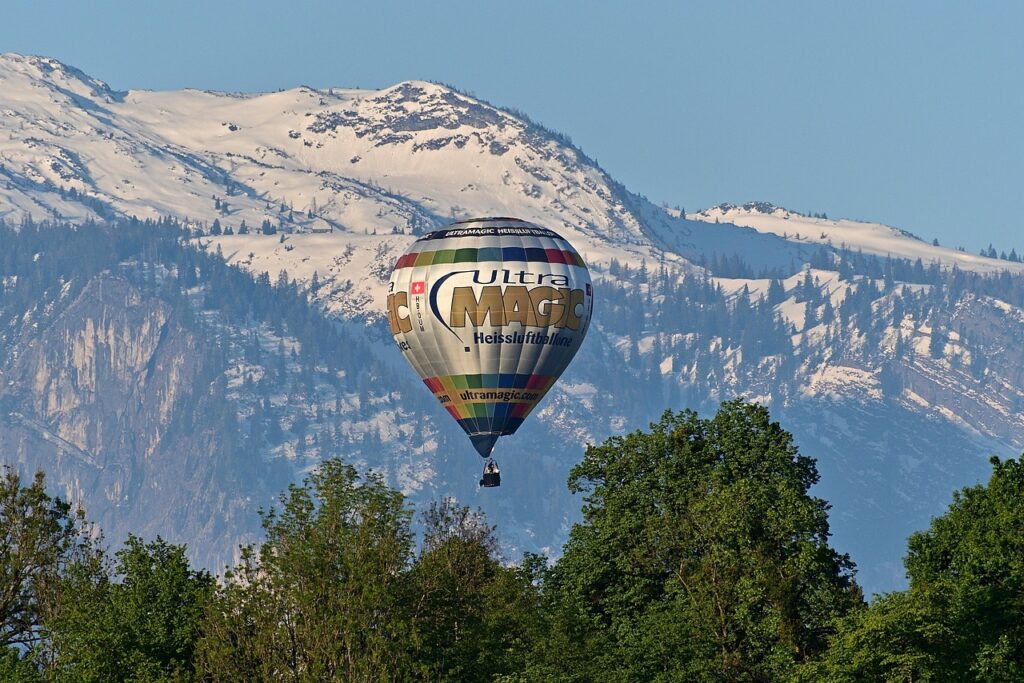 Une montgolfière colorée flotte majestueusement au-dessus de luxuriants arbres verts, avec des paysages du Maroc en toile de fond