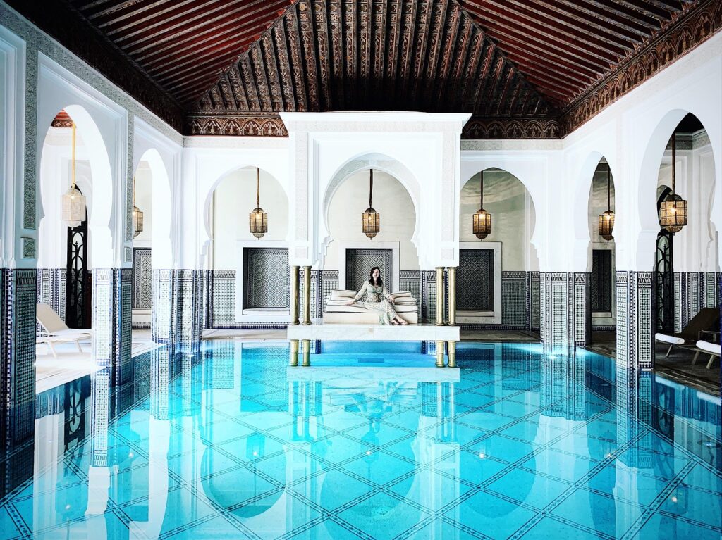 Une luxueuse piscine intérieure d'un Airbnb à Marrakech, avec une femme assise sur un banc au milieu de l'eau. 