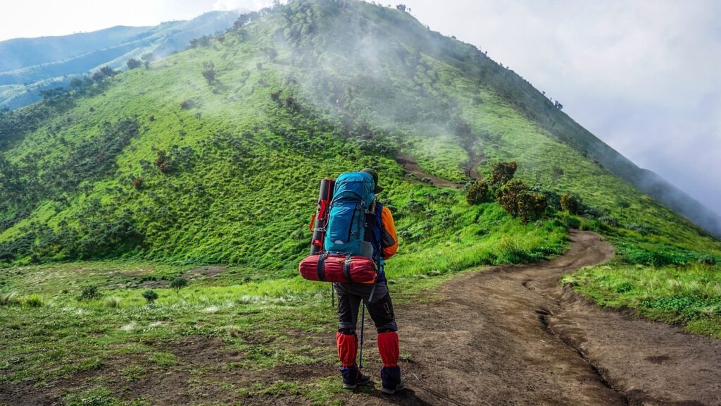 Randonneur portant un grand sac à dos coloré marchant sur un sentier de terre