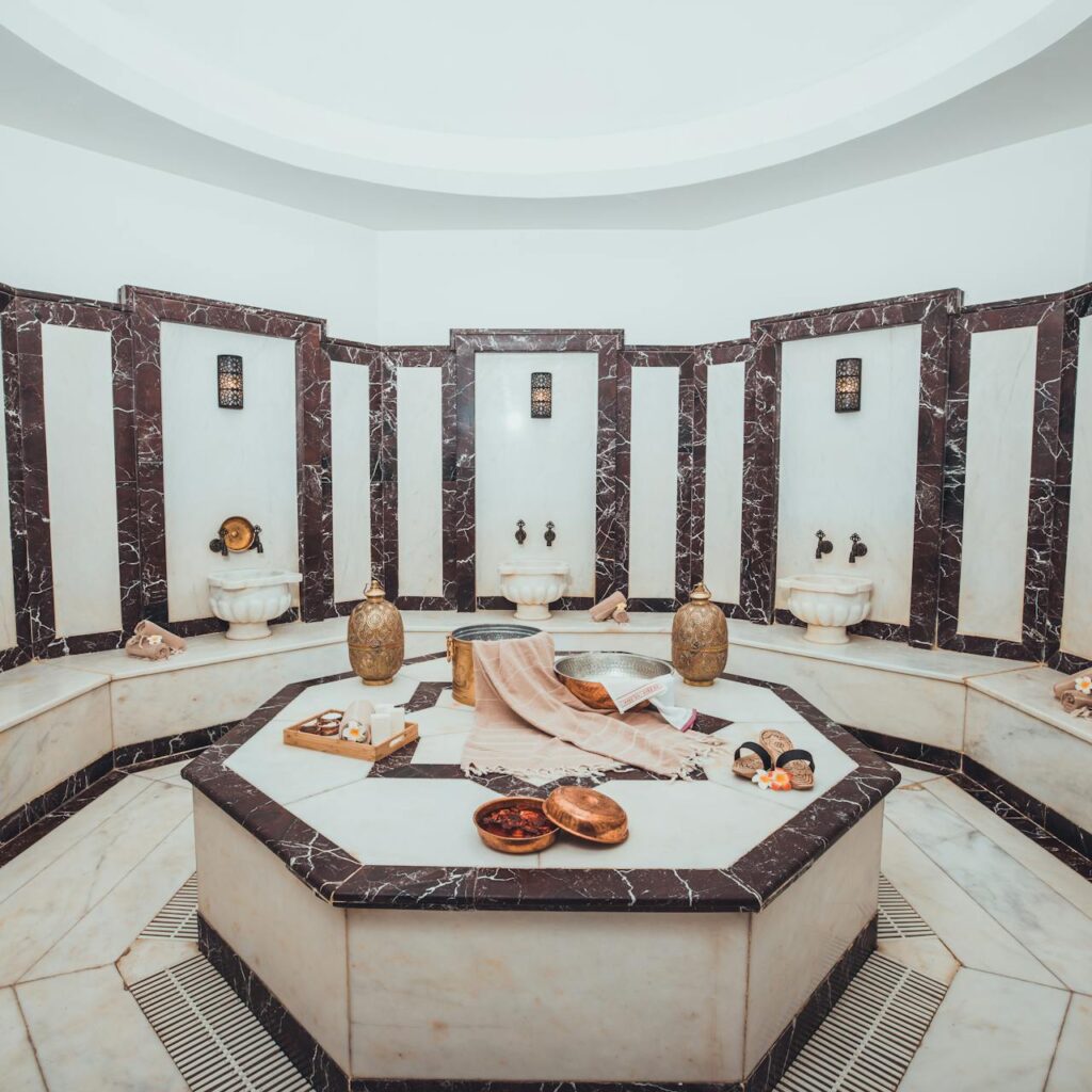 Hammam marocain élégant en marbre blanc et noir, décoré de lampes en laiton, bassins muraux et accessoires de bain traditionnels