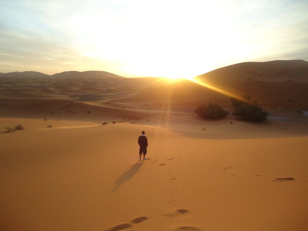 Une personne marche seule sur les dunes dorées du désert marocain au coucher du soleil,
