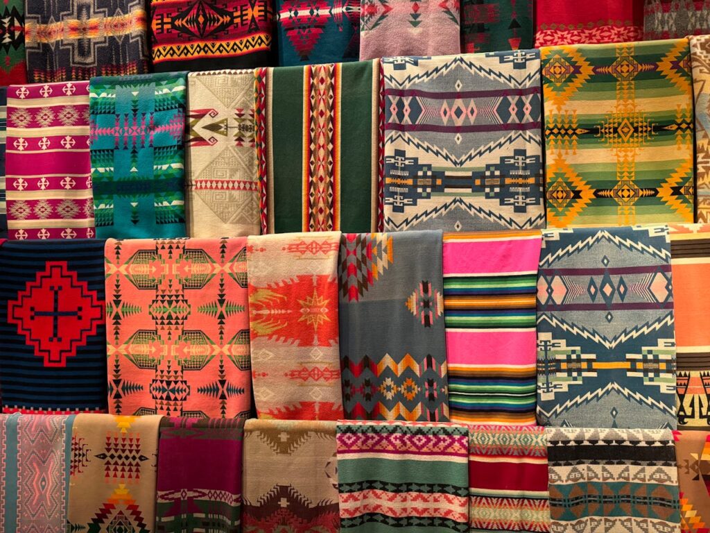 Collection de tapis marocains colorés exposés côte à côte, ornés de motifs géométriques et ethniques vibrants dans des tons de rouge, bleu, vert, rose et jaune, illustrant l’artisanat traditionnel du Maroc