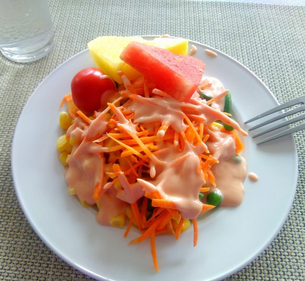 Salade marocaine végétarienne avec carottes râpées, maïs, tomate cerise, fruits frais et sauce crémeuse.