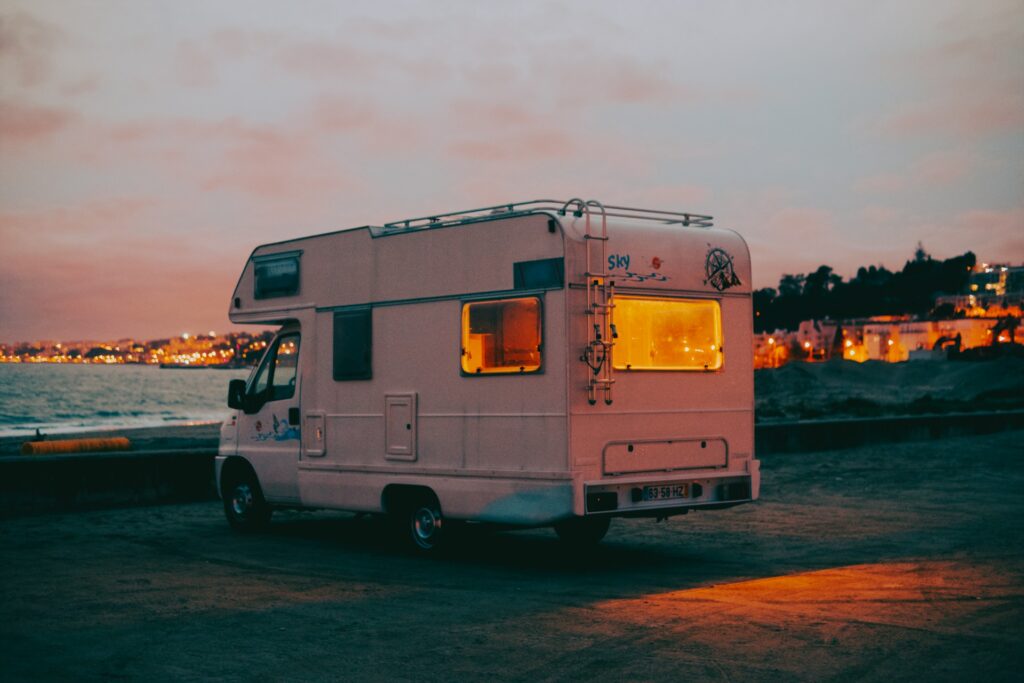 Un camping-car stationné au bord de la mer au crépuscule, avec ses fenêtres arrière illuminées. Prévoir un budget détaillé pour un voyage d’un mois au Maroc en camping-car

