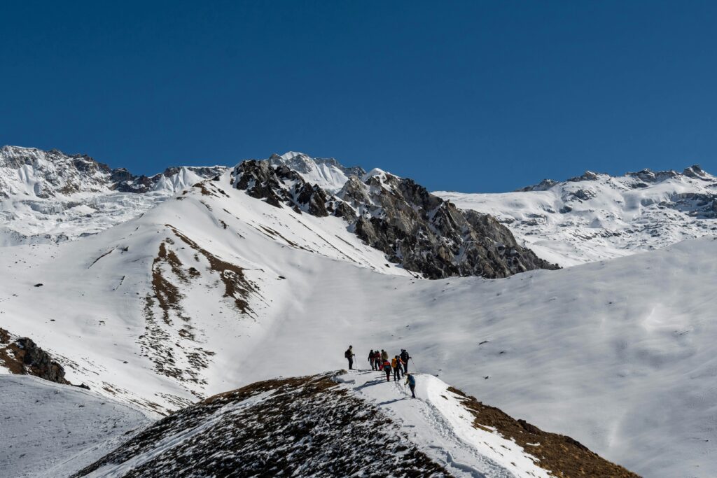 Cette image montre un groupe de randonneurs qui marchent sur un sentier au pied d'une montagne. Le sentier mène à un col qui offre une vue sur une vallée en contrebas, où se trouve le village berbère d'Imlil. 