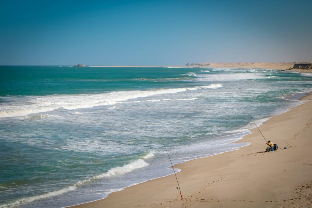 Une vaste plage de sable fin et doré s'étend le long d'une mer turquoise et agitée, illustrant parfaitement les plus belles plages du Maroc.