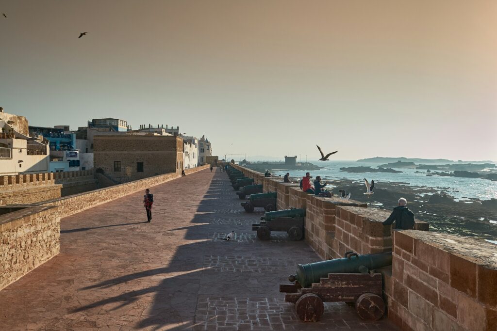 Vue panoramique des remparts historiques de la Sqala au coucher du soleil, où des résidents profitent de la douceur de l'océan Atlantique, illustrant la sérénité d'une retraite à Essaouira.