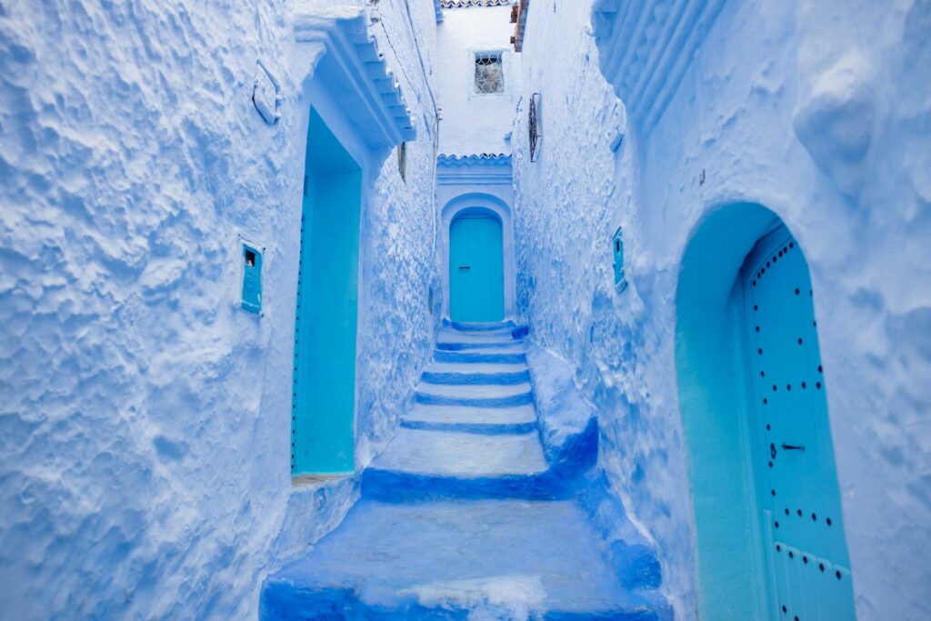 Une ruelle étroite et pittoresque de la médina de Chefchaouen au Maroc, entièrement peinte de nuances de bleu vif et de bleu ciel, créant une atmosphère captivante, typique d'un Voyage Tanger Chefchaouen à la découverte de la célèbre "Perle Bleue".