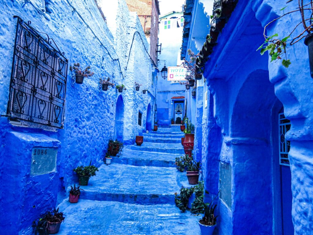 Une ruelle en pente et en escalier au cœur de la médina de Chefchaouen, baignée dans un bleu indigo intense et vibrant. Une scène pittoresque qui illustre le charme authentique d'un Voyage Tanger Chefchaouen à travers les montagnes du Rif.
