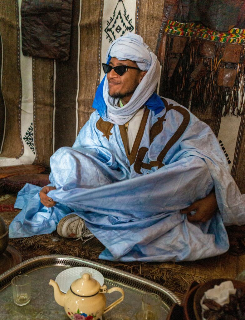 Un homme assis en tailleur à l'intérieur d'une tente traditionnelle, incarnant à la perfection l'hospitalité et le charme des rencontres camping-car Maroc 