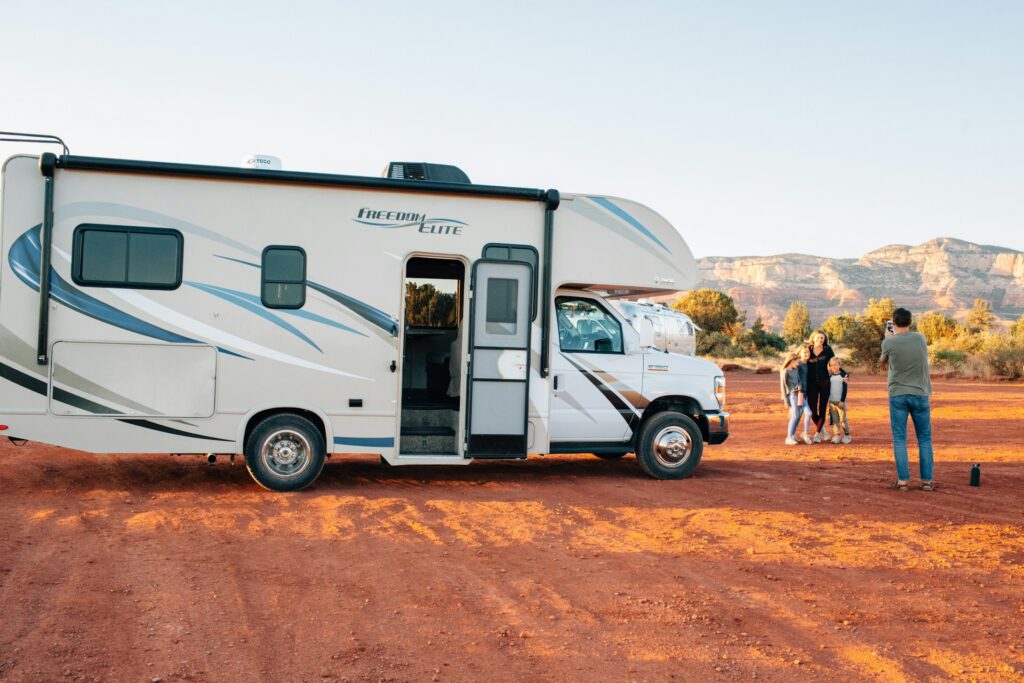 Famille profitant d’un moment convivial devant son camping-car lors d’un Voyager en famille au Maroc en camping-car. Dans un paysage désertique aux couleurs chaudes, parents et enfants immortalisent leur aventure nomade au coucher du soleil.