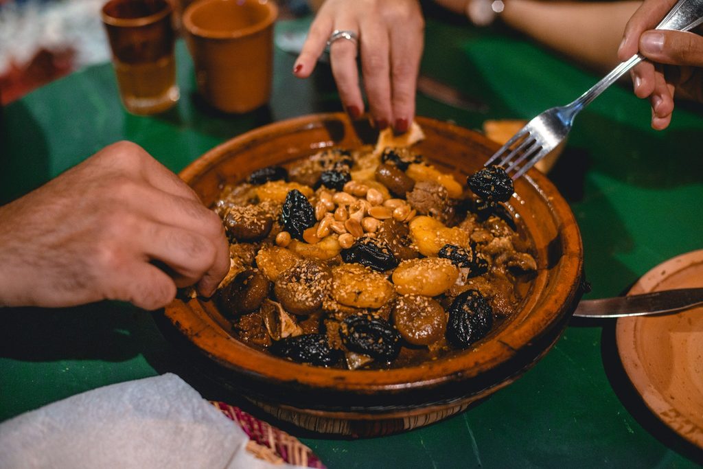 Dégustation conviviale d’un tajine aux pruneaux, amandes et sésame pendant une **Visite gastronomique à Marrakech**.
