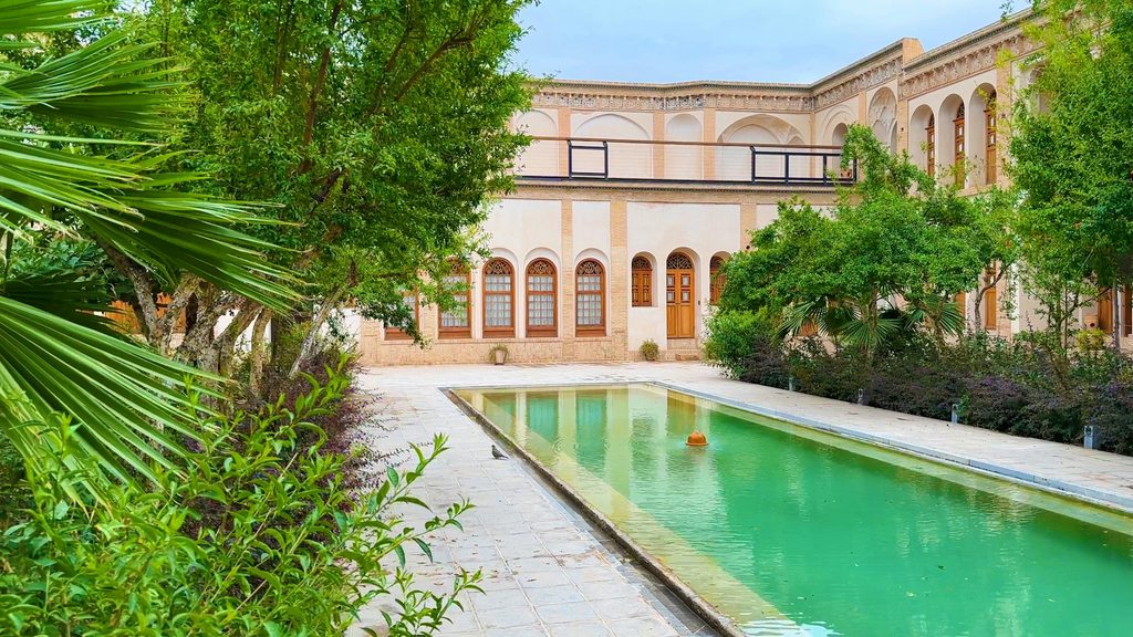 Découvrez les Riads au Maroc grâce à ce magnifique patio verdoyant avec grand bassin turquoise, arbres luxuriants et architecture traditionnelle.
